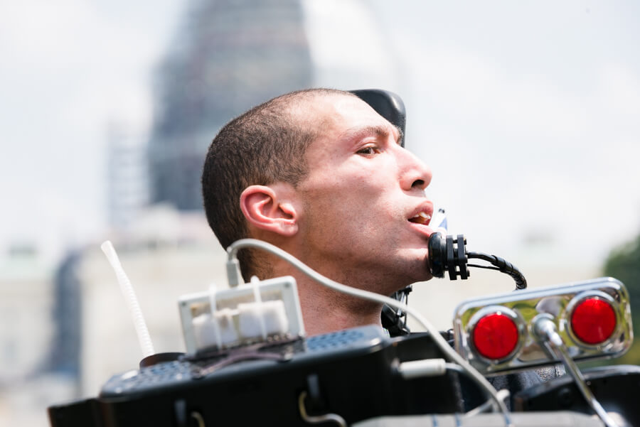 A man with close shaven brown hair using a chin control on a power wheelchair looks off to the side.