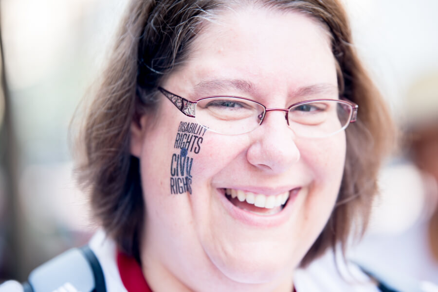 A close up on Sarah Launderville's face with a "Disability rights are civil rights" temporary tattoo on her cheek.