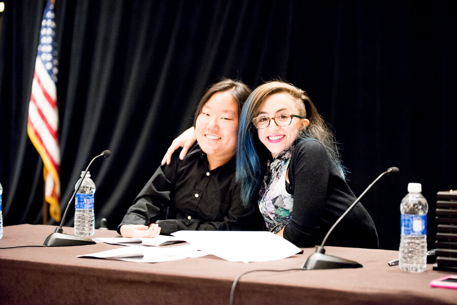Parker Glick, an Asian advocate with short dark brown hair, and Allie Cannington, a white woman with brown hair with blue streaks, smile with their arms around each other.