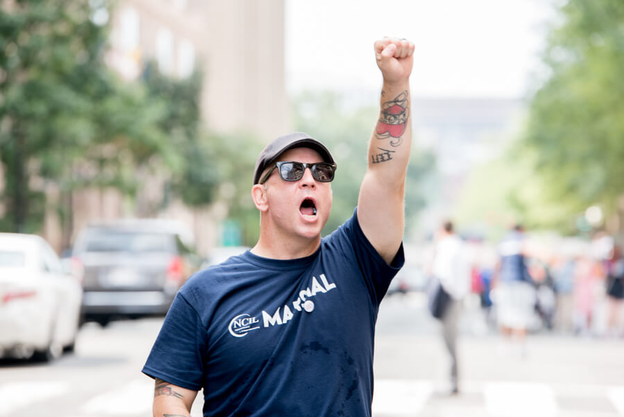 A man dressed in a NCIL Marshal shirt shouts with a fist raised.