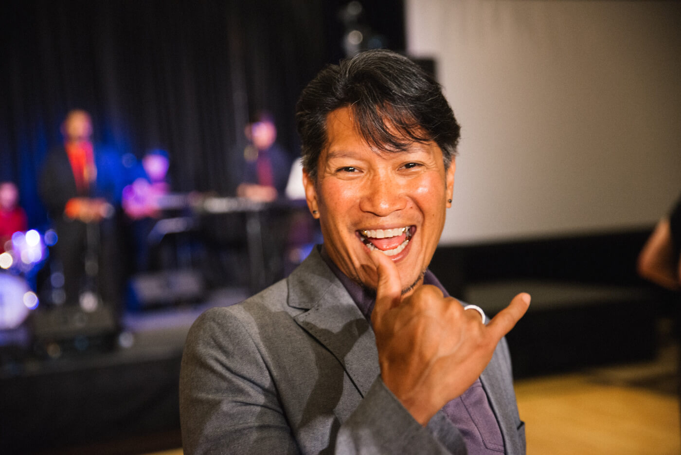 An advocate with medium brown skin smiles open mouthed at the camera and does a Y handshape during NCIL's closing dance.