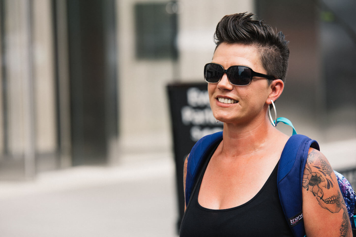 A person with short black hair with shaved sides, sunglasses, hoop earrings, and a skull tattoo on their upper arm marches during NCIL's annual march.