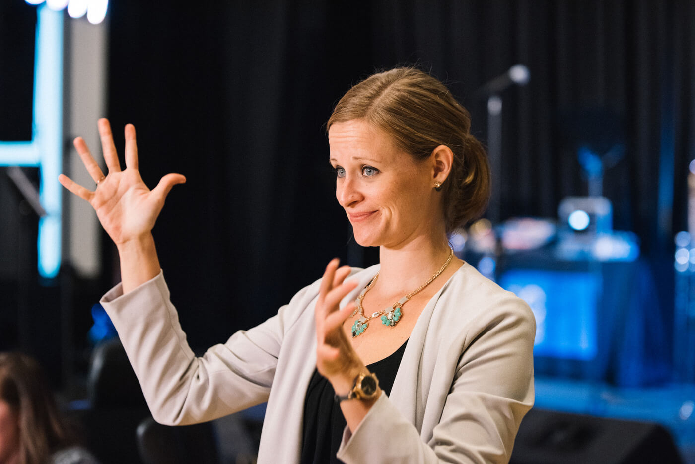 A white woman with dark blonde/light brown hair pulled back into a ponytail signs applause.