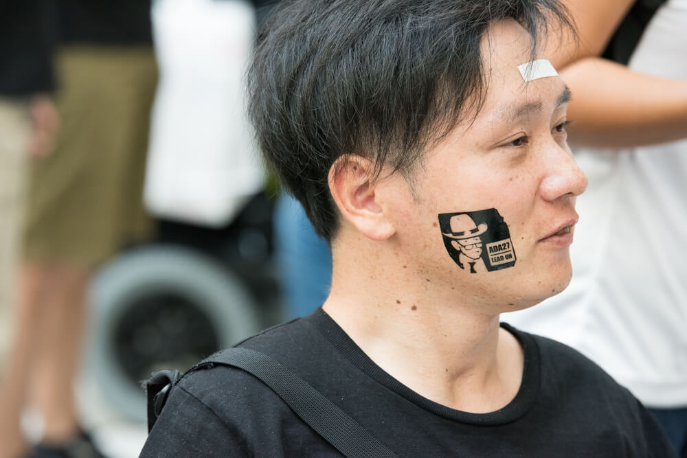 A side view of a Japanese advocate with a temporary tattoo of Justin Dart on their cheek.