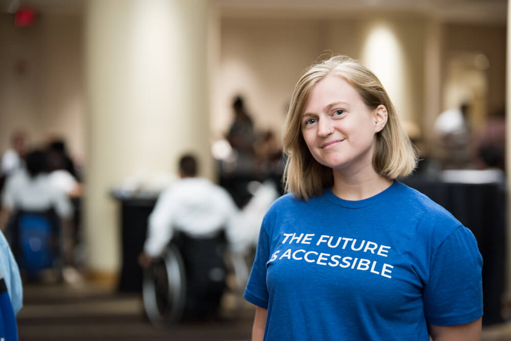 An advocate wears a t-shirt that says "The Future is Accessible" and smiles at the camera.