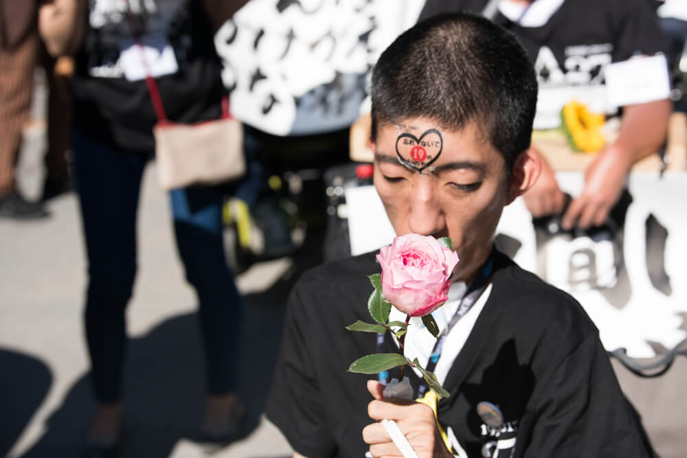 A Japanese advocate with a temporary tattoo on their forehead of a heart sniffs a flower during NCIL's annual march and rally.