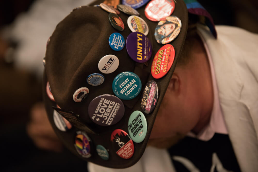 A close up of buttons on an advocate's hat that say things like "Every woman counts." "Unity!" and "Vote" with the O replaced with a wheelchair heart symbol.