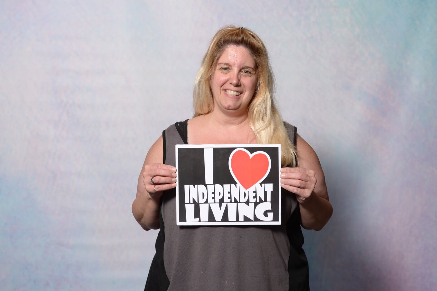 A person smiles at the camera holding a sign that says "I [heart] Independent Living".