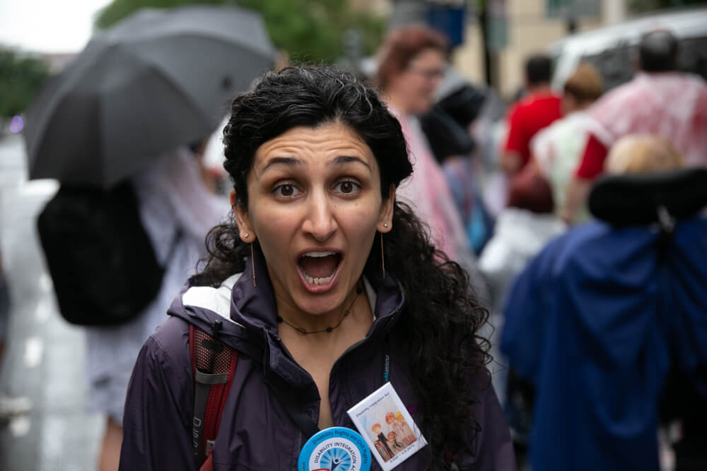 An advocate marching in the rain looks at the camera with open-mouthed joy.