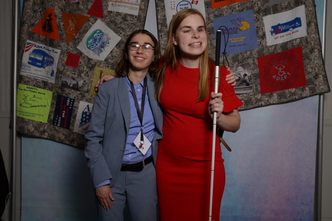 Melissa Carney and Eryn Star stand with their arms around each other in front of the ADA quilt backdrop.