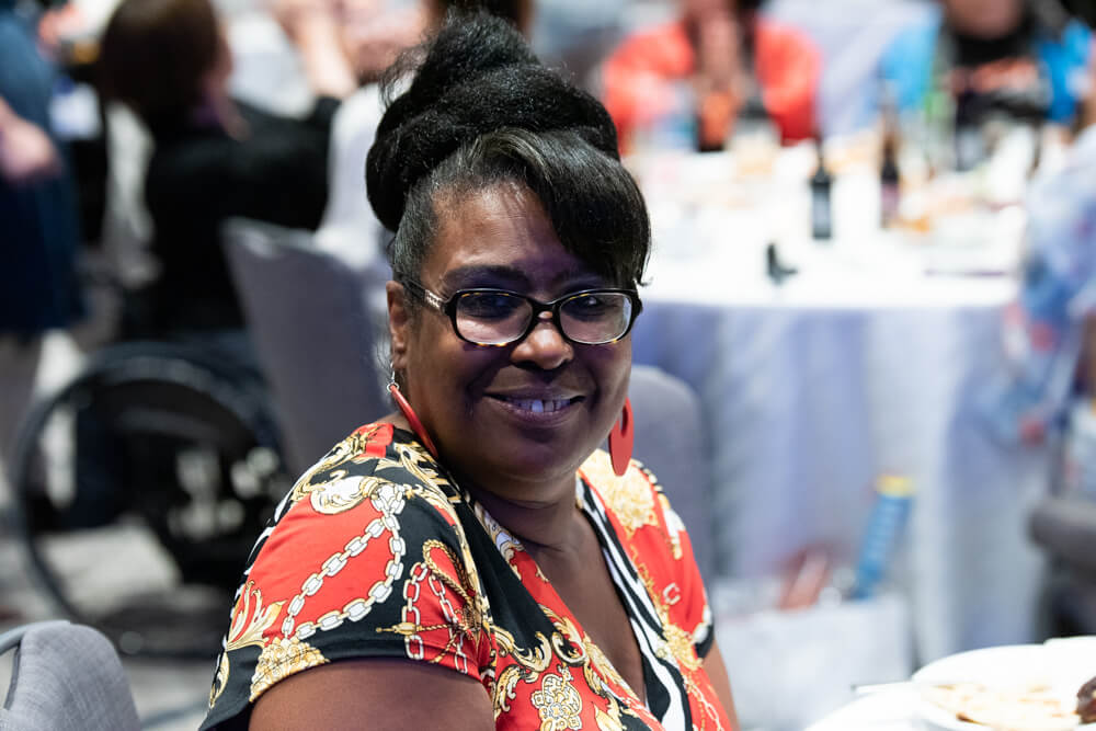 Denise Law, a Black woman with black hair pulled up into a ponytail, smiles at the camera.