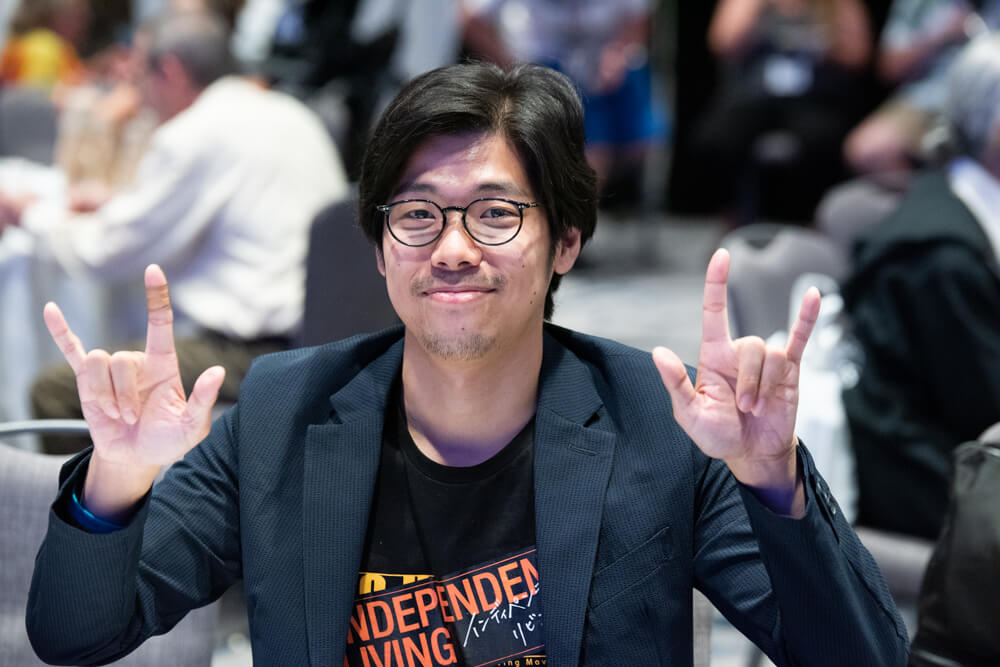 A white man with short black hair and glasses shows double "I love you" signs to the camera.