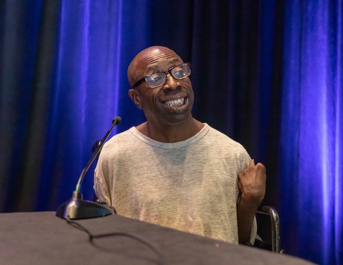 Keith Jones, a Black bald advocate using a wheelchair, speaks into a microphone.
