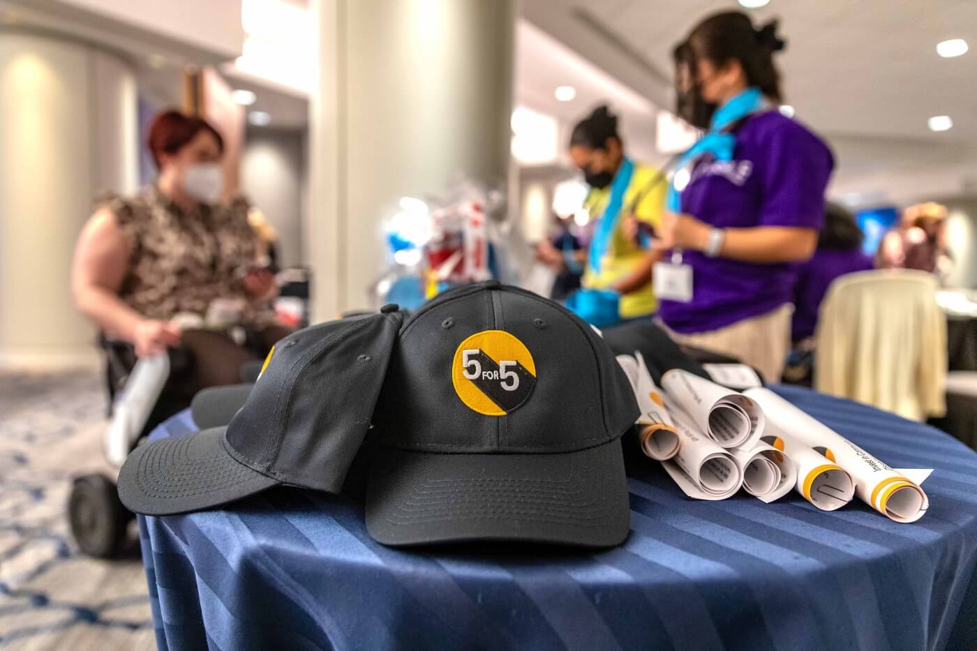 Rolled up poster kits and 5 for 5 hats sitting on a small table.
