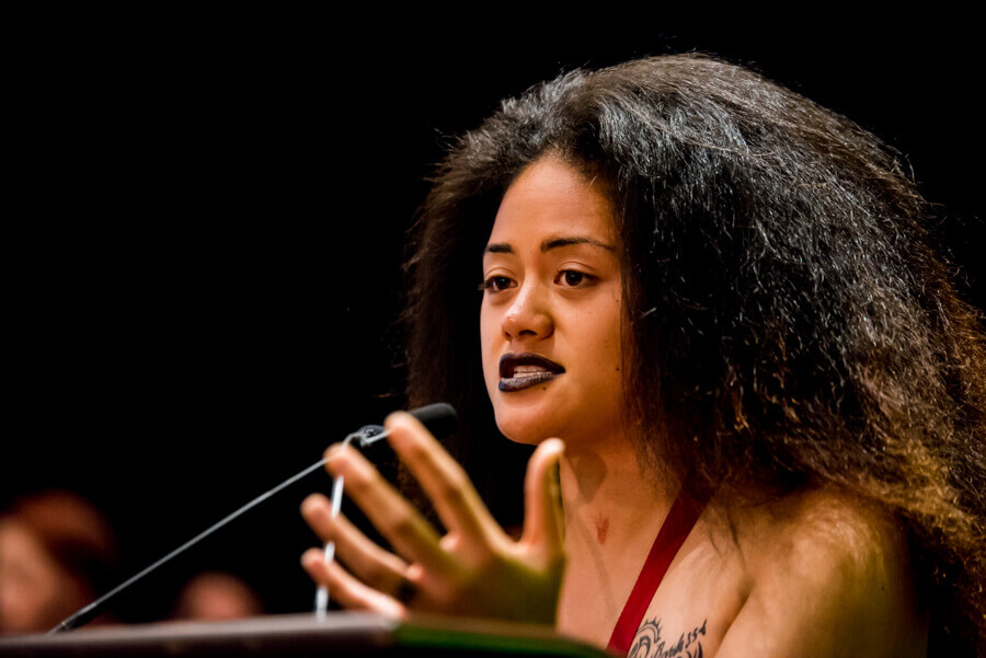 Tangikina Moimoi speaks into the microphone from the stage at the Annual Conference