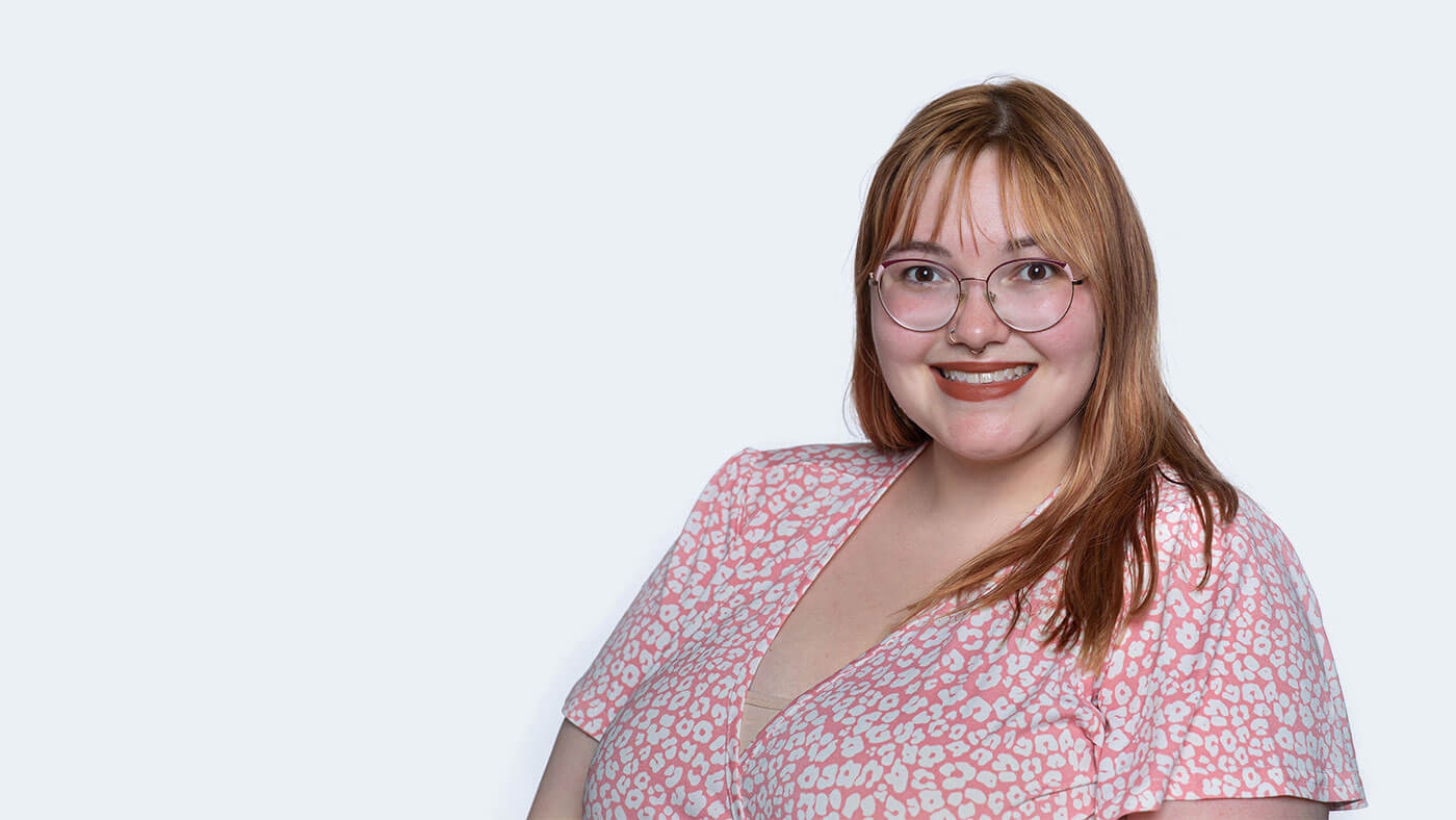 Brianna Zimmerman, a white person with glasses and reddish blonde hair just past the shoulders, smiles at the camera.