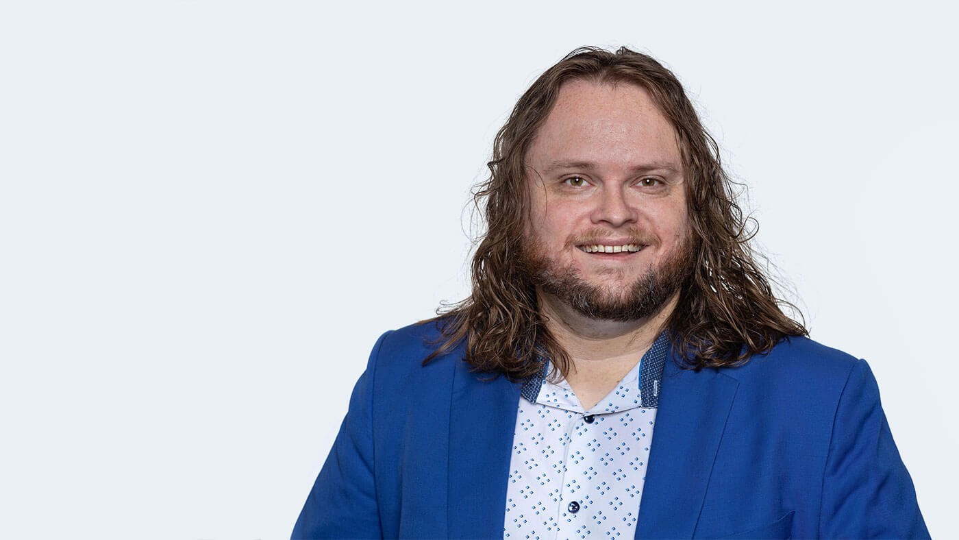 Colin Killick, a white man with shoulder length brown hair, smiles at the camera.