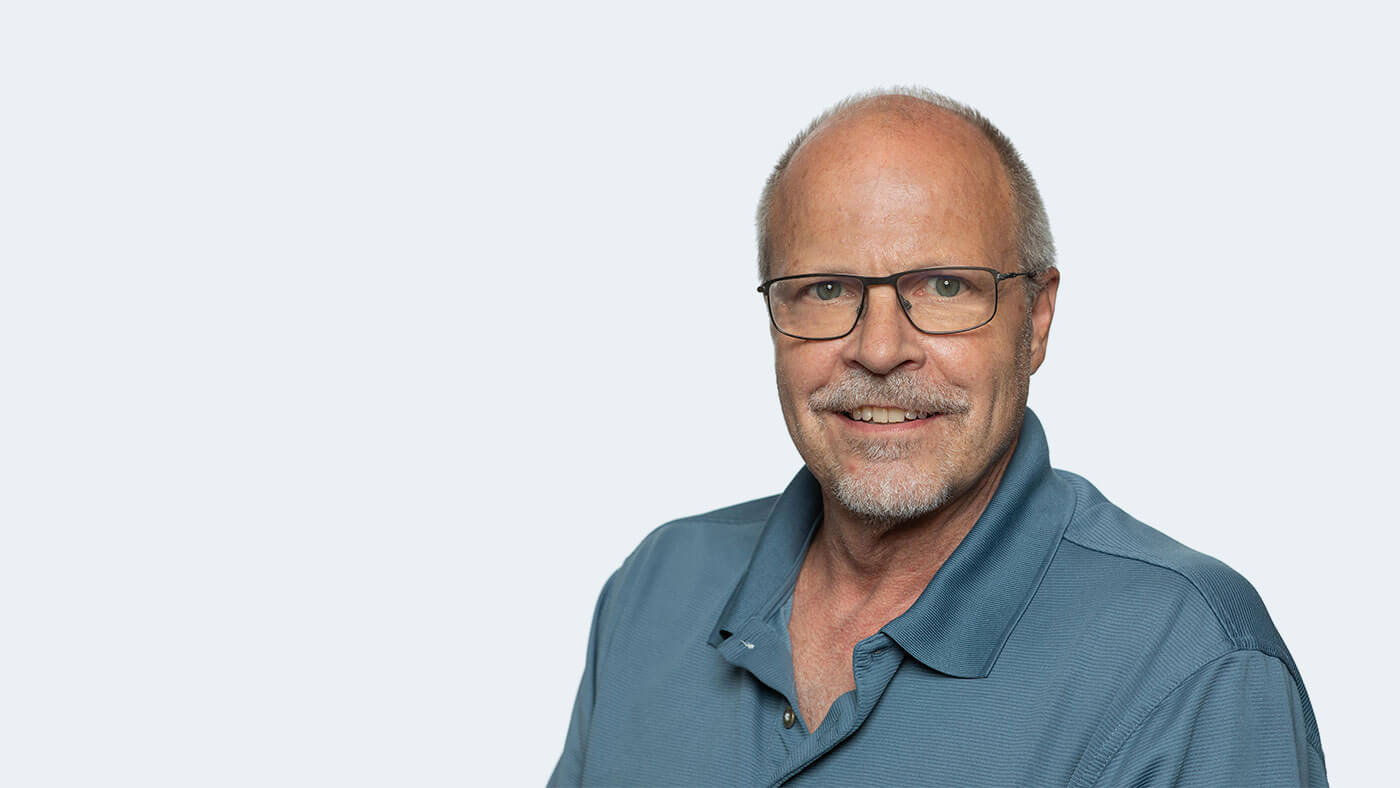 Dan Ashbaugh, a white man with greyish stubble, short hair, and glasses smiles at the camera.