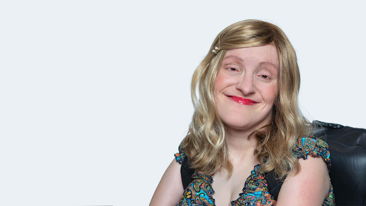 Elizabeth Brassell, a white woman with shoulder length wavy blonde hair and bright red lipstick, smiles at the camera with head tilted.