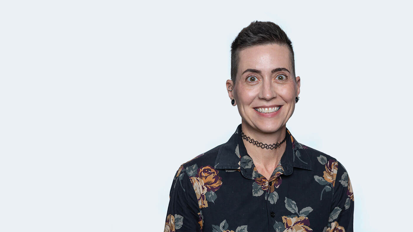 Farrah Garland, a white person with short black hair and a black choker necklace, smiles at the camera.