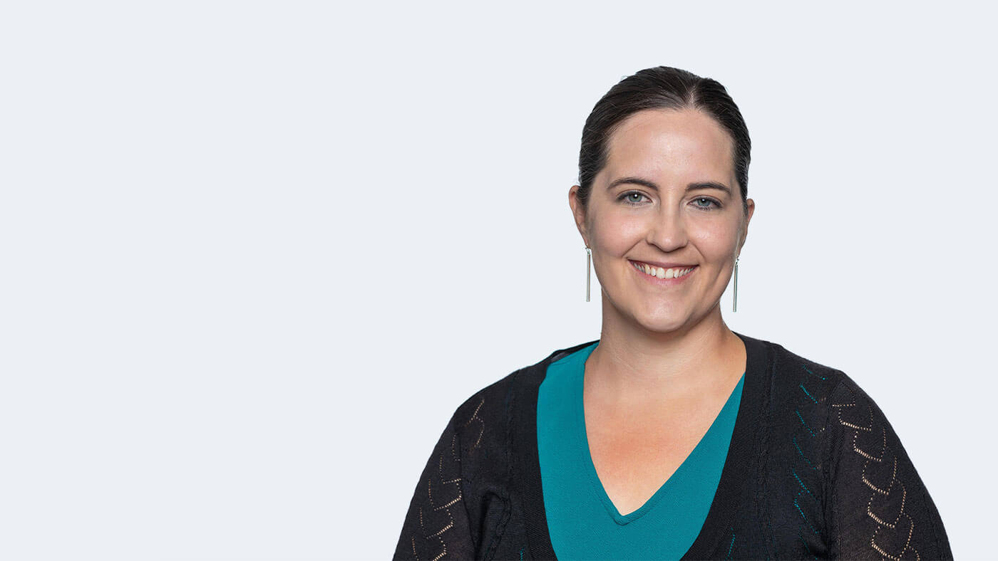 Heather Kamper, a white person with dark brown hair in a ponytail and long silver earrings, smiles at the camera.