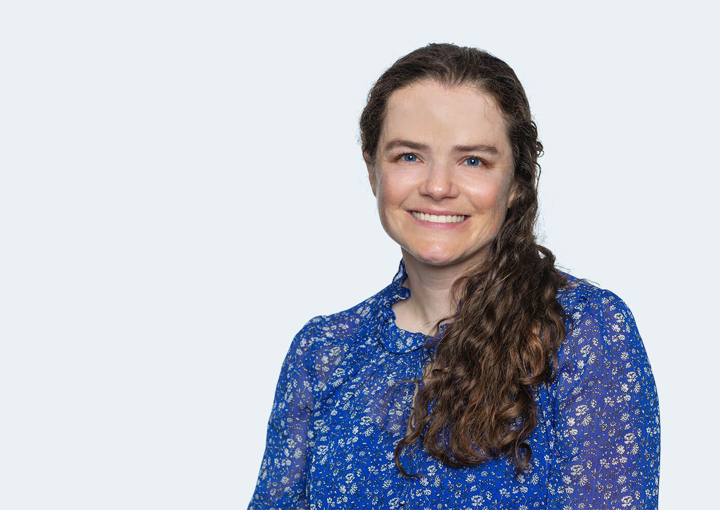 Jenny Sichel, a white person with brown curly hair in a side ponytail, smiles at the camera.