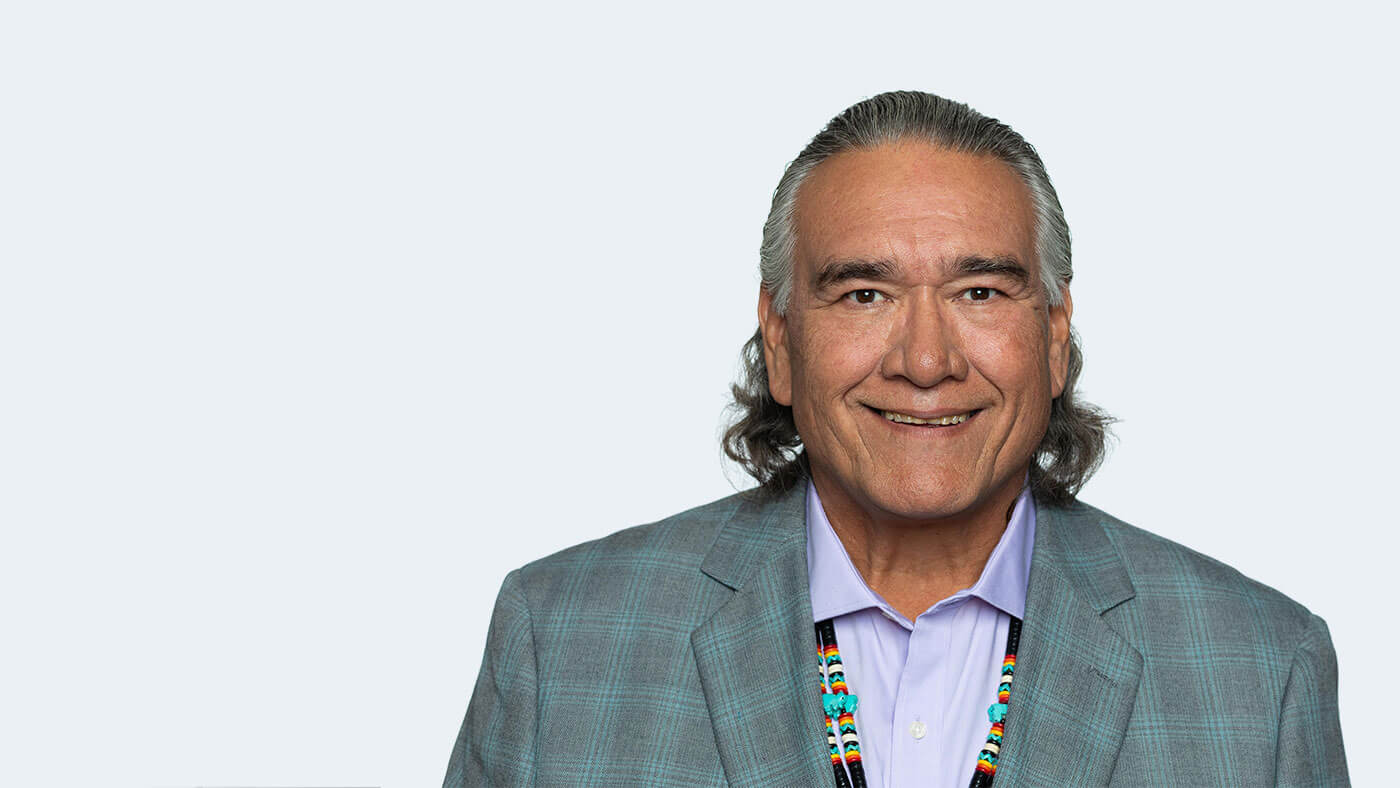 Jim Warne, a Native American person with short grey hair, smiles at the camera.