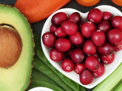 Bowl of grapes in a heart-shaped bowl next to avocados and squash on a table.