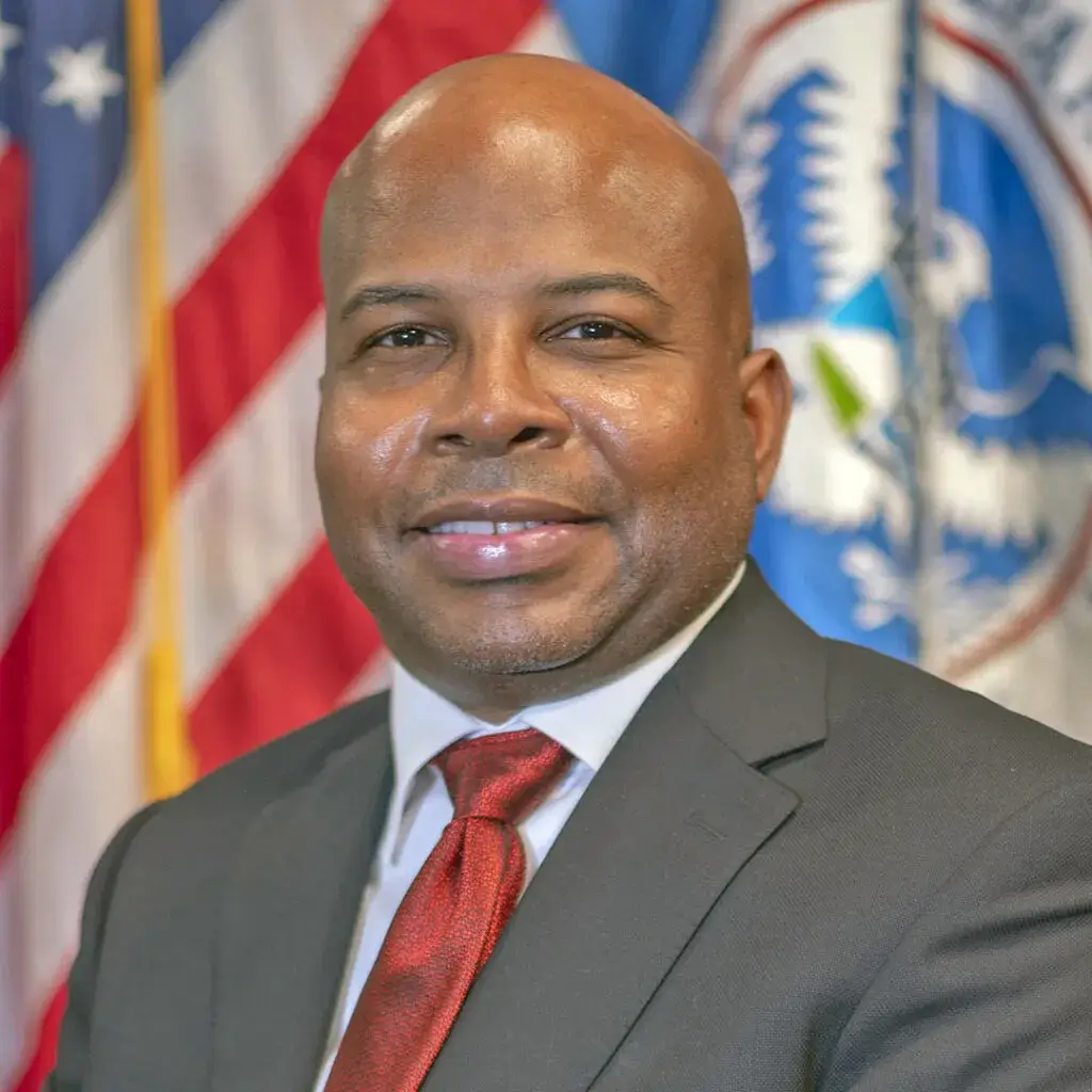 Sherman Gillums, Jr. poses for an official head shot with the U.S. Flag behind him