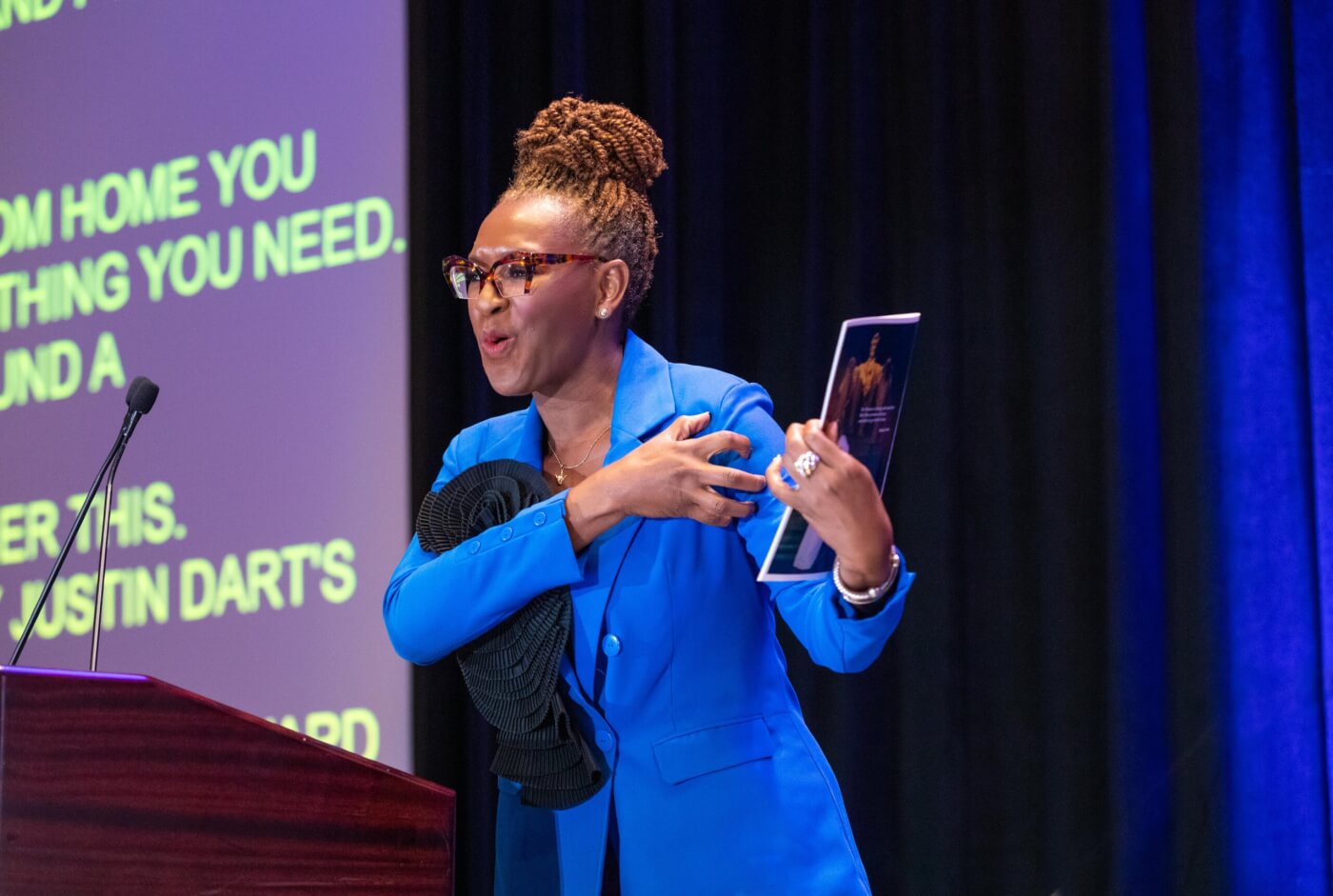 Claudia Gordon accepting the Max Starkloff Lifetime Achievement Award. Claudia is standing at a podium on stage signing “power” in American Sign Language.