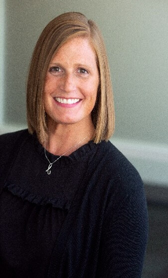 white female with dark blonde hair wearing a black shirt and a silver B necklace
