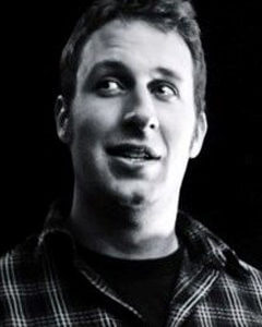 A Black and White image of a white 40 year old male in a button up collared shirt smiling and looking to his right.