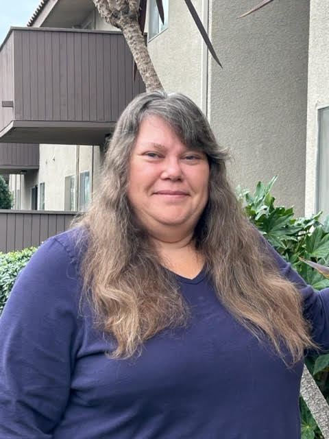 A photo of a middle-aged white woman with long brown hair, smiling for the camera.