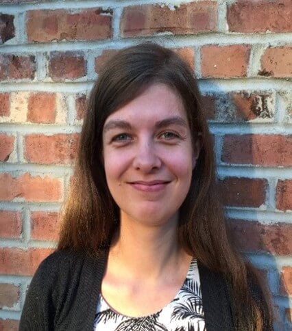 white female with light brown hair wearing a black sweater over a white and black flower printed top.