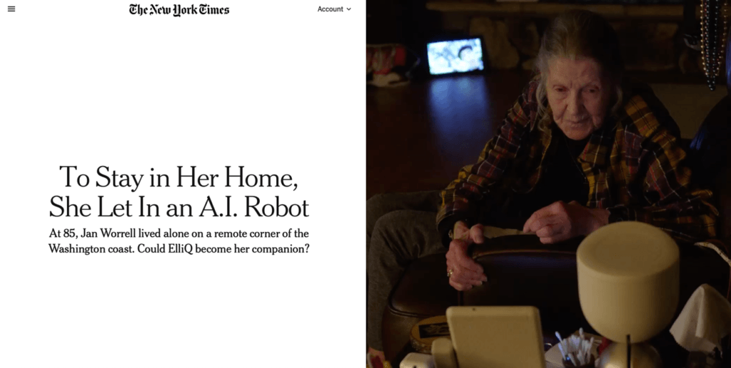 Photograph showing an elderly woman sitting in a dimly lit room, interacting with a cylindrical A.I. robot on a table. The context highlights companionship technology for seniors, focusing on Jan Worrell, who lives alone and uses the ElliQ robot to stay connected and engaged.