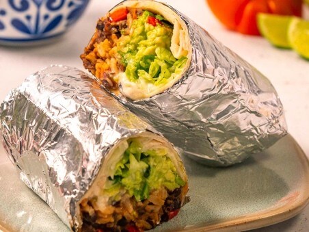 A photo of a burrito wrapped in foil. You can see tortilla and a bit of filling, rice and guacamole.