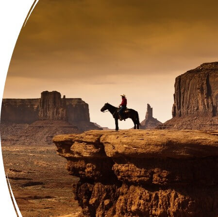 Horseback rider on desert butte. In the background is another mountain that is far away.